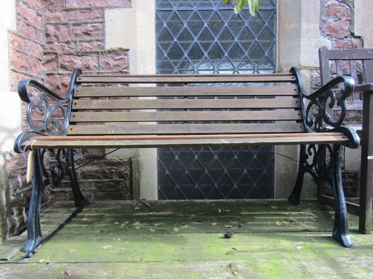 A two seat garden bench with timber lathes and decorative pierced cast iron ends, 130 cm long