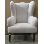 An Edwardian wing armchair with simply upholstered light oatmeal fabric and raised on square tapered