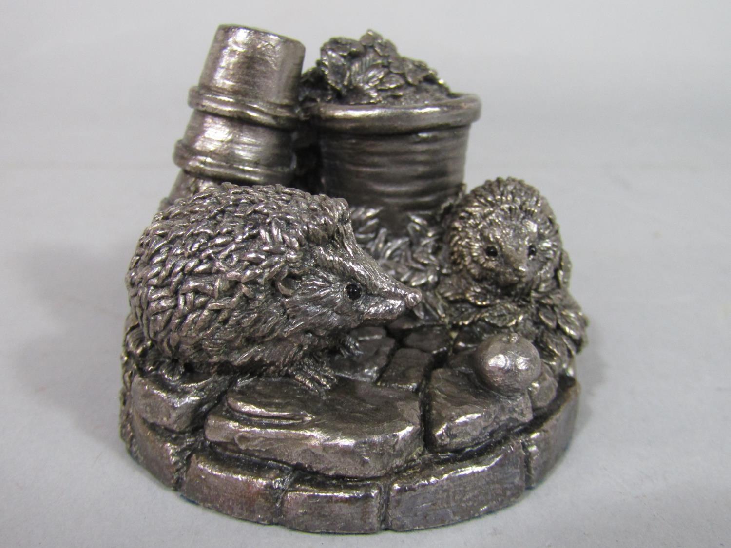 A silver applied character group of two hedgehogs amongst flowerpots in a garden setting, signed