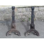 A pair of heavy cast iron andirons with face mask and gothic tracery detail, 52 cm high