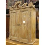A small stripped pine hanging wall cupboard enclosed by a pair of fielded panelled doors beneath a