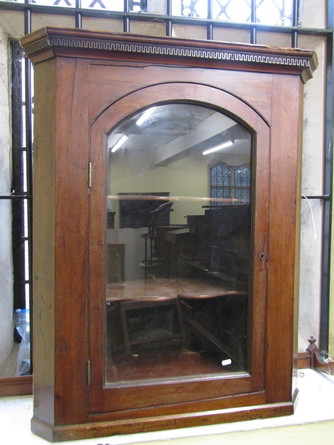 A 19th century mahogany hanging corner cupboard enclosed by an arched and glazed panelled door,