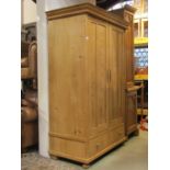 A continental stripped pine wardrobe enclosed by a pair of three quarter length panelled doors