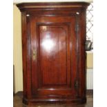 A Georgian oak country made hanging corner cupboard, the panelled door with simple floral