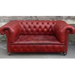 A small red leather two seat Chesterfield sofa with deep buttoned seat, back and rolled arms, raised