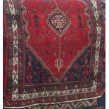 A Hamadan village rug with central blue medallion framed by various floral sprays upon a red ground,