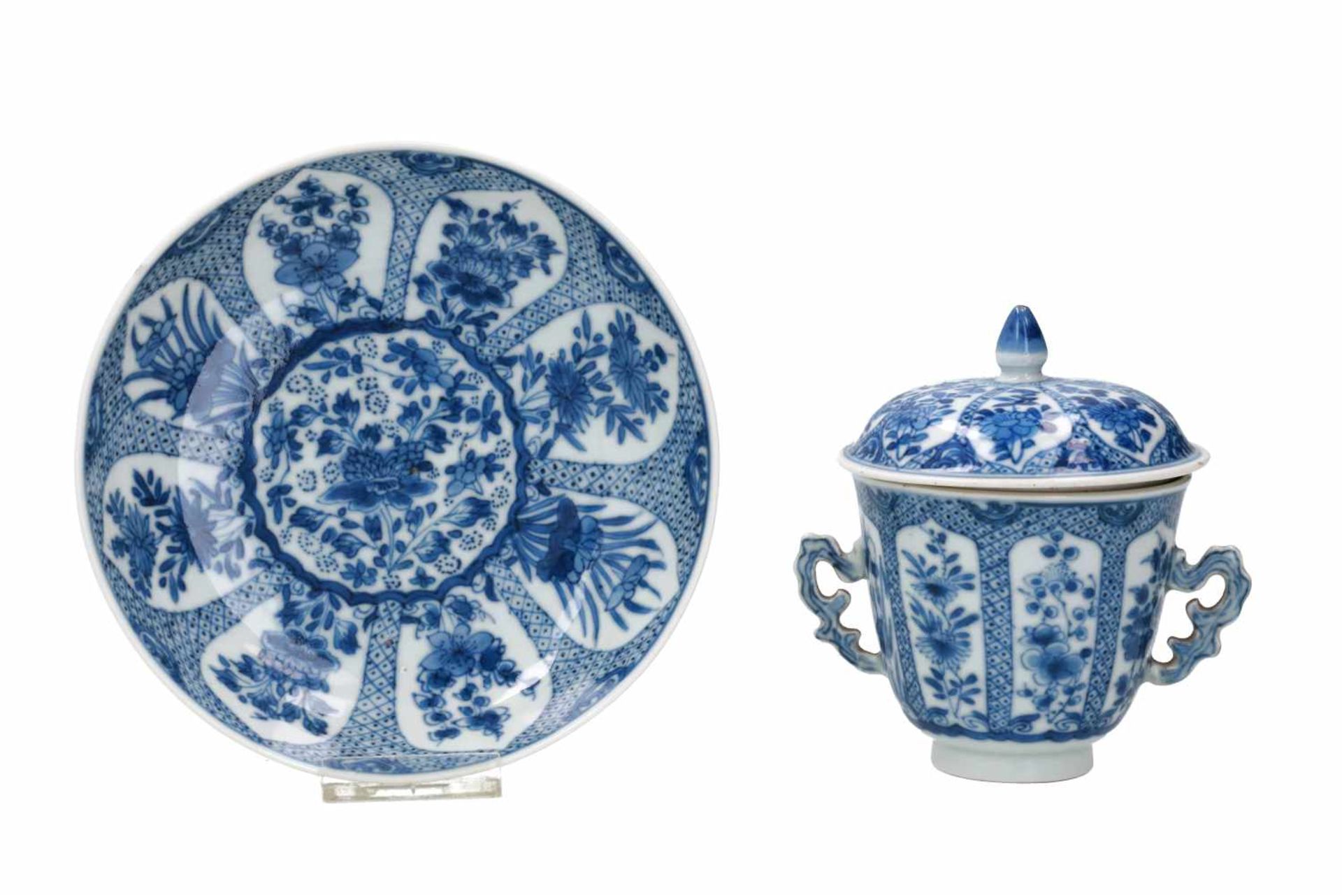 A blue and white porcelain lidded cup with two handles on a deep saucer, decorated with flowers.