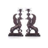 A PAIR OF BRONZE CANDLESTICKS IN THE FORM OF GRIFFINS Each seated figure with wings extended