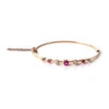 A GOLD BANGLE Claw-set to the centre with an old-cut ruby, flanked on each side by an alternating