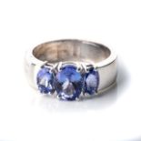 A TANZANITE TRILOGY RING Claw-set to the centre, with an oval-cut tanzanite weighing approximately