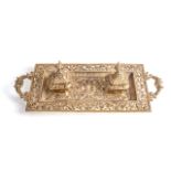 A FRENCH BRASS DOUBLE INKWELL DESKSET With ornate detail, two inkwells with hinged lids, on
