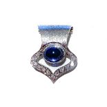 A SAPPHIRE AND DIAMOND ENHANCER cantered by an oval cabochon bezel set sapphire weighing