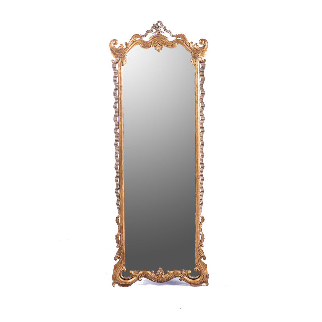 A GILT MIRROR The shaped rectangular plate within a conforming frame, surmounted by a ribbon
