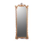A GILT MIRROR The shaped rectangular plate within a conforming frame, surmounted by a ribbon