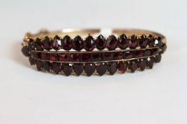Early 20th Century Garnet set hinged bangle, mounted with a row of channel set square cut Garnets, a