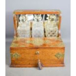 A late 19th century oak tantalus, containing three cut glass decanters, with games box to the front,
