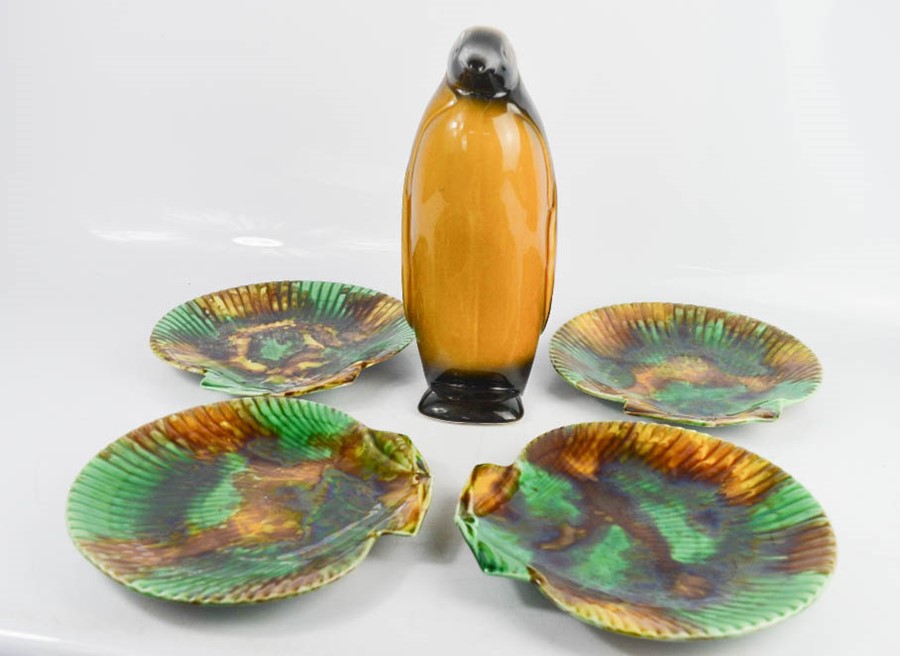 A group of shell form plates, in green and brown glaze, together with a ceramic penguin.