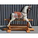 A painted rocking horse, dapple grey, with tan saddle, and pine base.