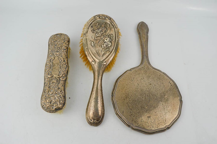 A silver hand brush, clothes brush embossed with scrollwork, and a hand mirror engraved with