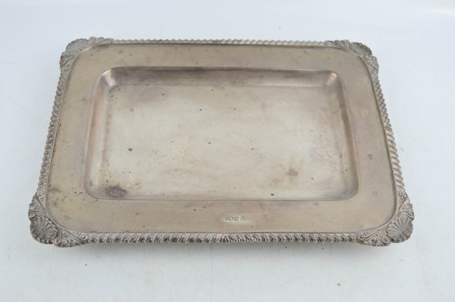 A silver rectangular dish raised on four bun feet, with scallop shells to the corners and decorative