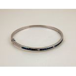 An 18ct white gold, sapphire and diamond set bangle, with 24 princess cut sapphires, and two