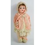 A German bisque headed late 19th / early 20th century doll, wearing a peach silk bonnet and cape,