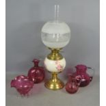 Three cranberry glass jugs and a bowl, together with a Victorian porcelain and brass parafin lamp,