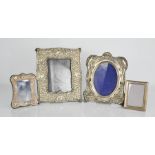 A group of four silver photograph frames, three embossed with decoration, the largest measures 21 by