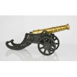 A brass cannon raised on a black painted cast frame. 22cms tall x 43cms long