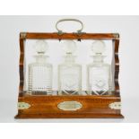 An oak tantalus containing three cut glass decanters, with key, bearing plaque inscribed to Mr JW