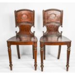 A pair of Regency mahogany hall chairs, early 19th century, bearing a crest to the backs, and raised