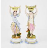 A pair of Victorian porcelain flower sellers with baskets raised upon their heads, 20cm high.