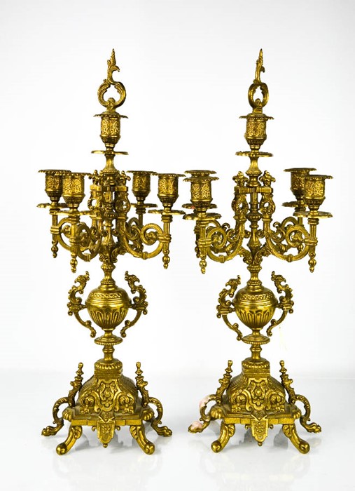 A pair of brass candleabra, with five candle sockets, raised on decoratively cast bases.