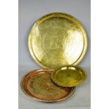 A large brass Indonesian tray top, together with a smaller example and a tray in copper.