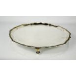 A silver circular tray by Mappin & Webb, Sheffield 1931, with a wavy edge, raised on four ball &