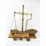 A pair of vintage brass scales, together with four sets of weights, raised on a wooden plinth.