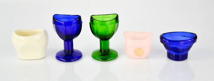 Five vintage eye baths, including three glass examples.