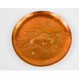 An Arts & Crafts Newlyn copper circular dish decorated with a fish and stylised waves and air