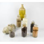 A group of vintage glass bottles with stoppers, each with contents labels, together with a stoneware