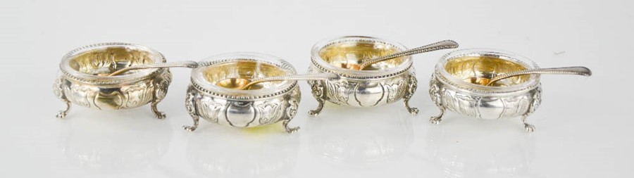 A set of four silver salts with clear glass liners and four salt spoons.