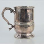 A Georgian polished pewter mug on a raised circular foot with scroll handle