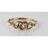 A 9ct rose gold antique "lovers knot" bangle with a hinged clasp and fitted safety chain, 10.4g