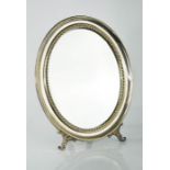 A continental white metal oval table mirror on Rococo style feet, 29 by 23cm.