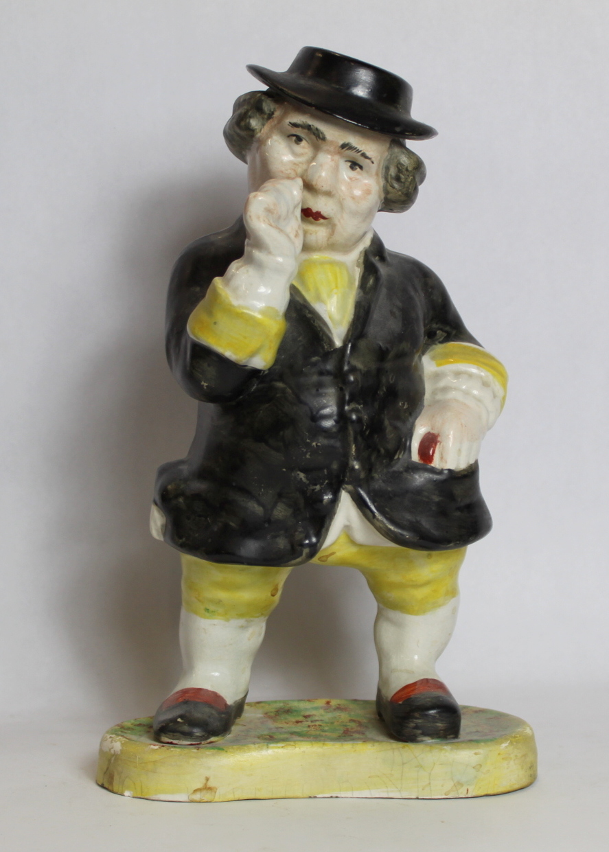 19th century pottery figure of a man taking snuff, standing on a kidney shaped plinth base,