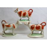 Three 19th century Staffordshire pottery cow creamers, all on oval plinth bases with iron red and