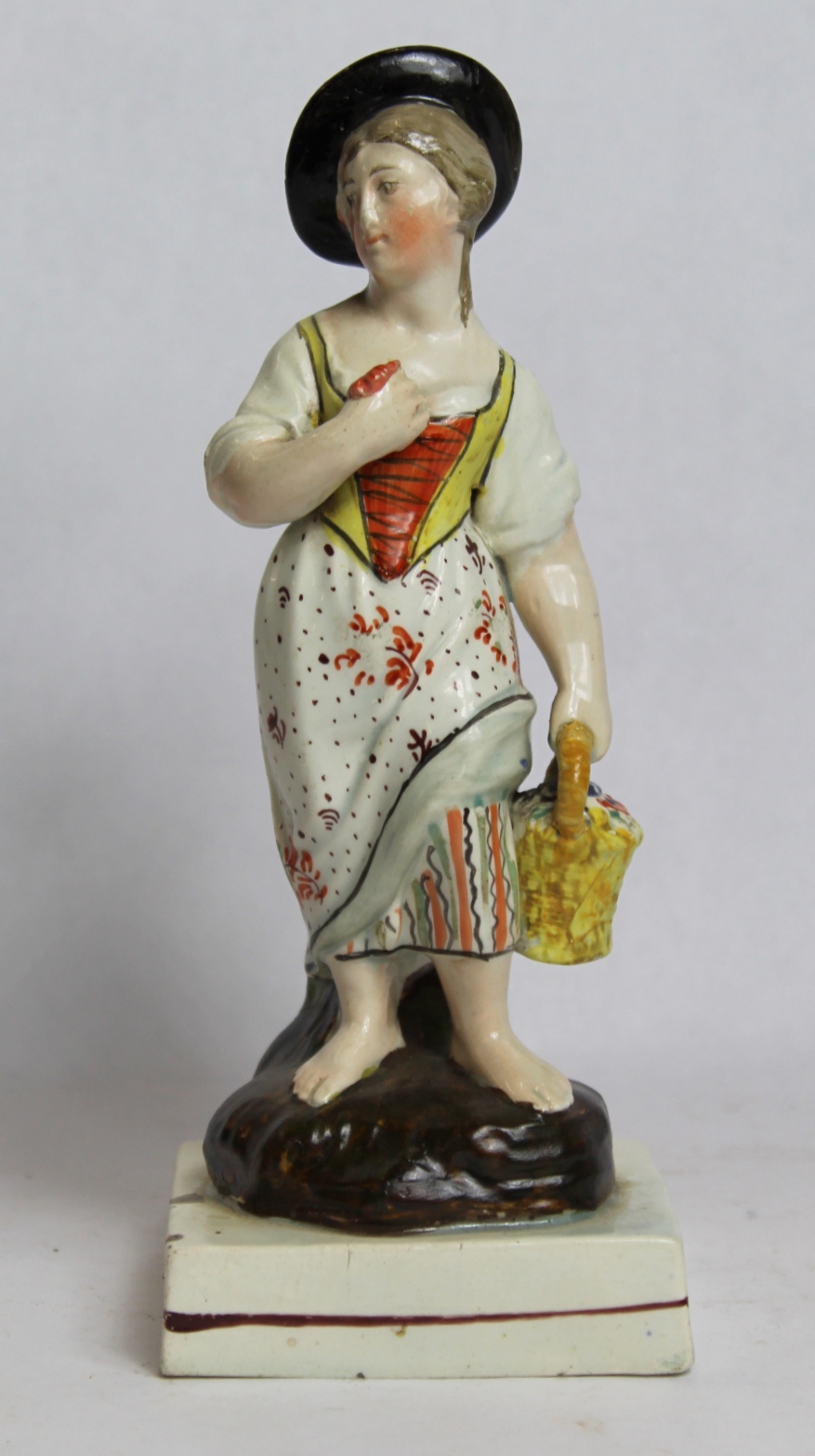 19th century pearlware figure of a farm girl carrying a basket of flowers, on square plinth base