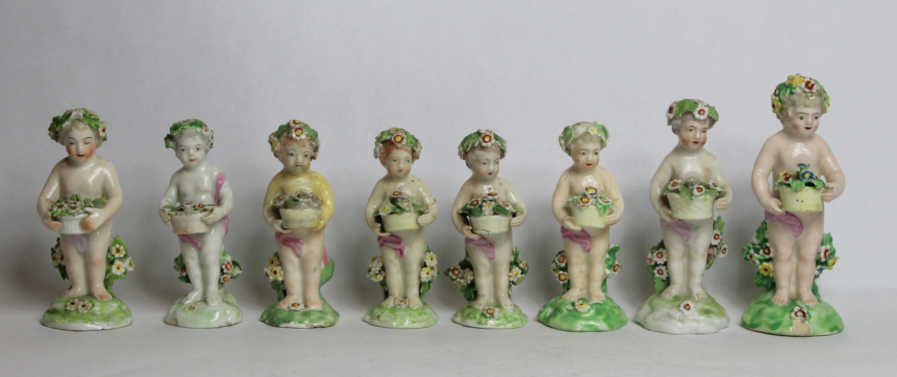 Seven 18th century Derby porcelain small figures of putti holding baskets of flowers, all with patch