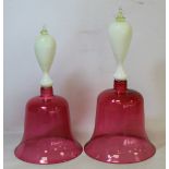 Two Victorian cranberry glass hand bells with cased opaque white finialled handles, 31cm and 28cm