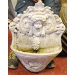 Composite wall fountain with floral back plate and cherub masks over basin, 56cm wide and 74cm high;