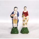Pair of Portobello style pottery figures, each holding a basket of harvest fruits, label for DM &